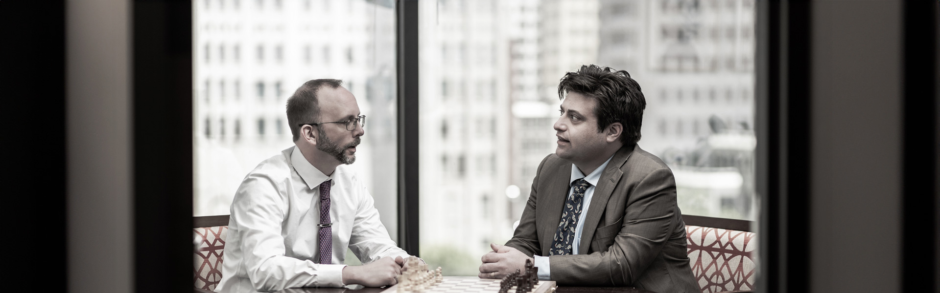 Mark Hennelly and Johnathon Brereton-Hubbard sit at a conference room table talking over a chess board